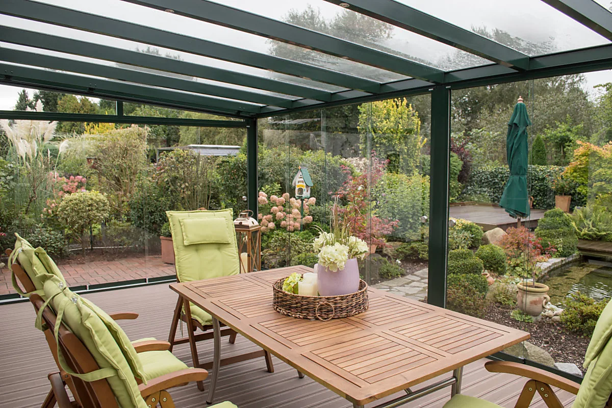 Lichtdurchflutete verglaste Terrasse mit Holztisch und Blick auf blühenden Garten